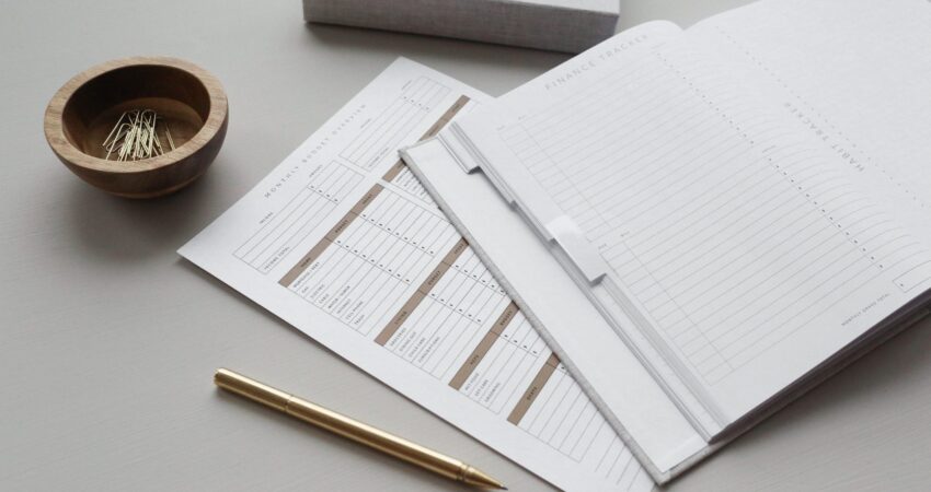 Ein Finanzplaner in Buchform neben einer Schale Büroklammern und einem Kugelschreiber